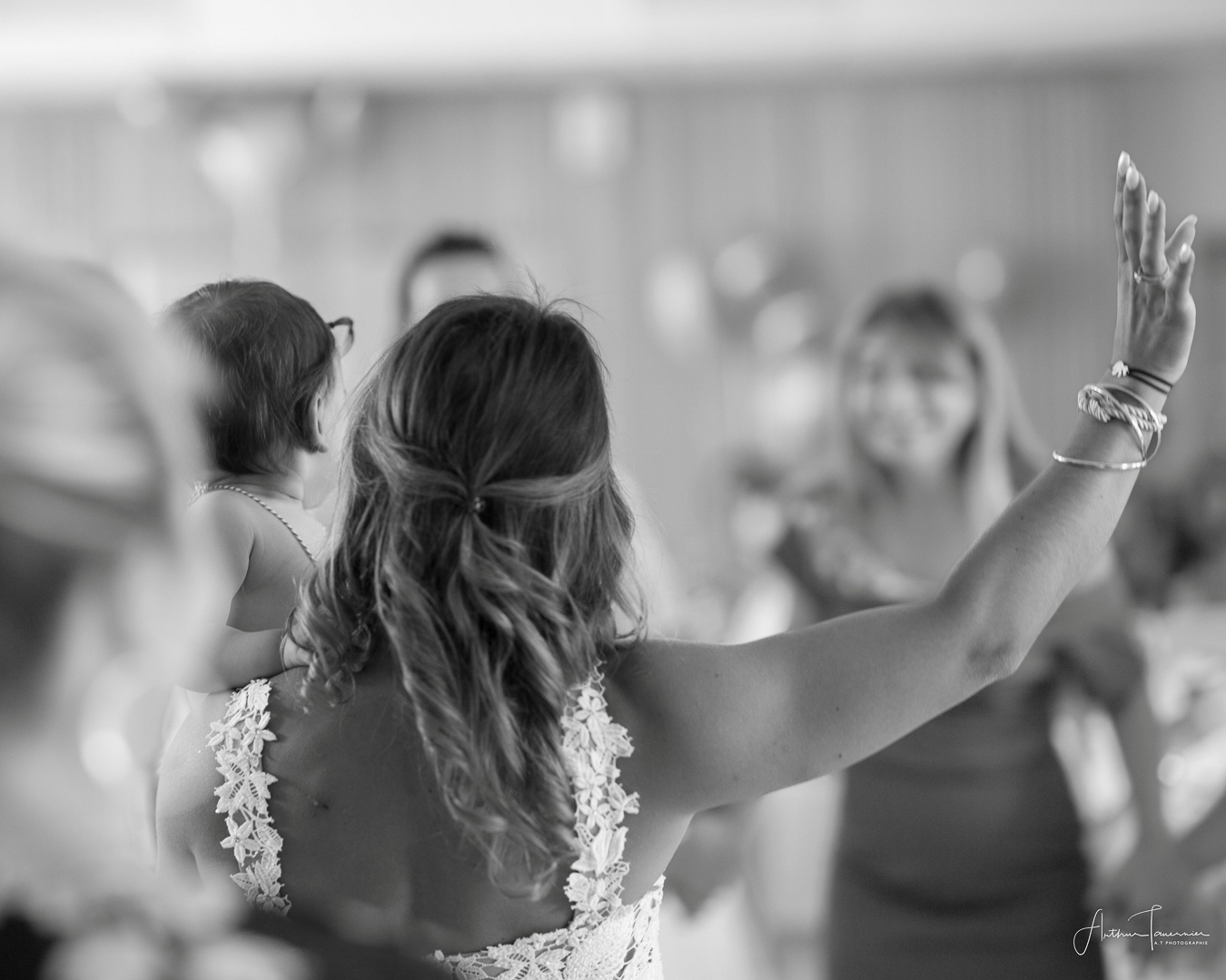 Femme en robe blanche de mariée tenant un enfant lors d'un moement de célébration, photographié sur le vif en noir et blanc.